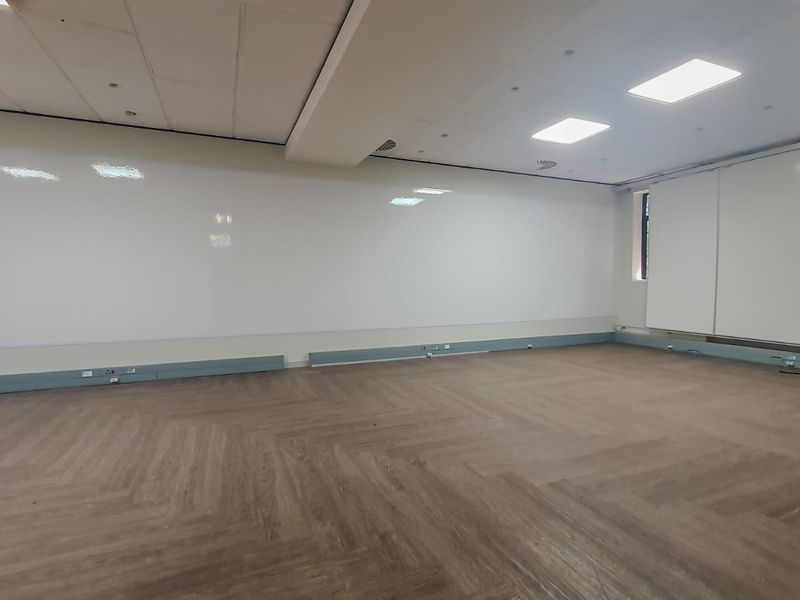 A spacious, empty commercial office area featuring modern herringbone vinyl flooring, recessed ceiling lighting, and a large integrated whiteboard wall.