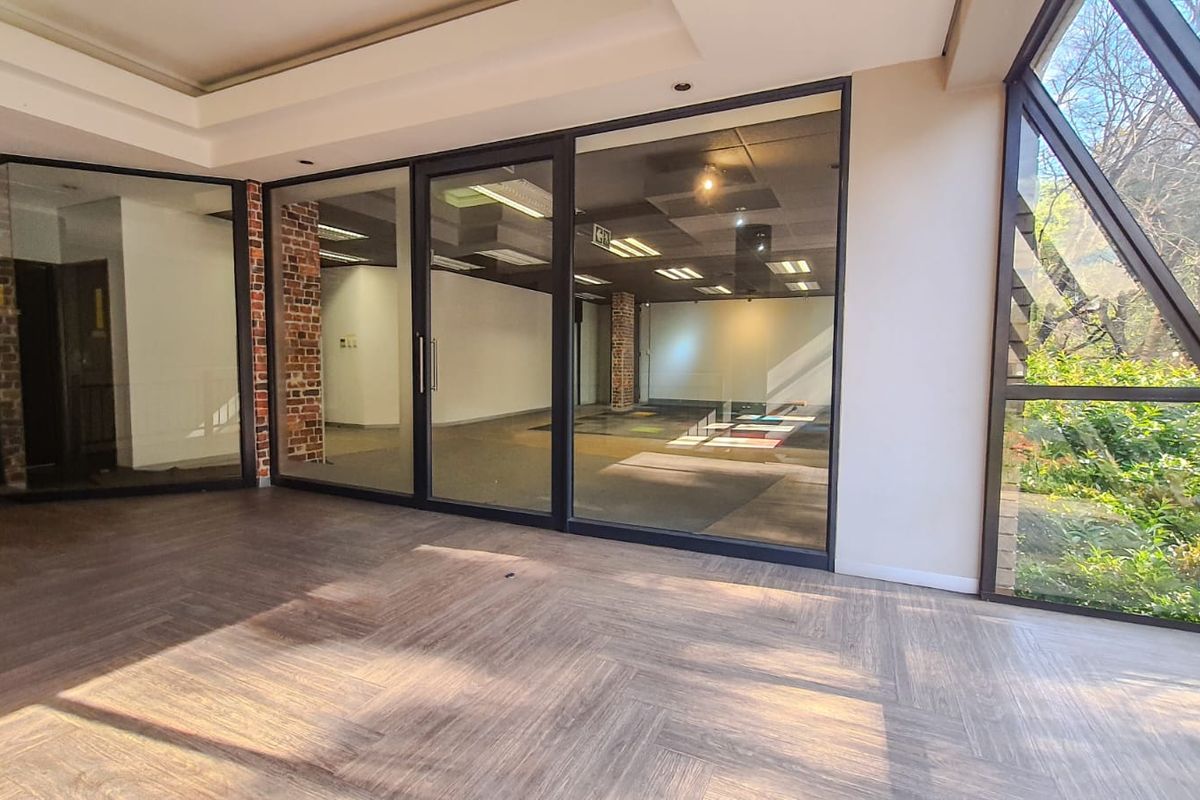 Modern, vacant commercial office space featuring herringbone flooring, exposed brick accents, and large glass partitions providing excellent natural light and an open, professional atmosphere.