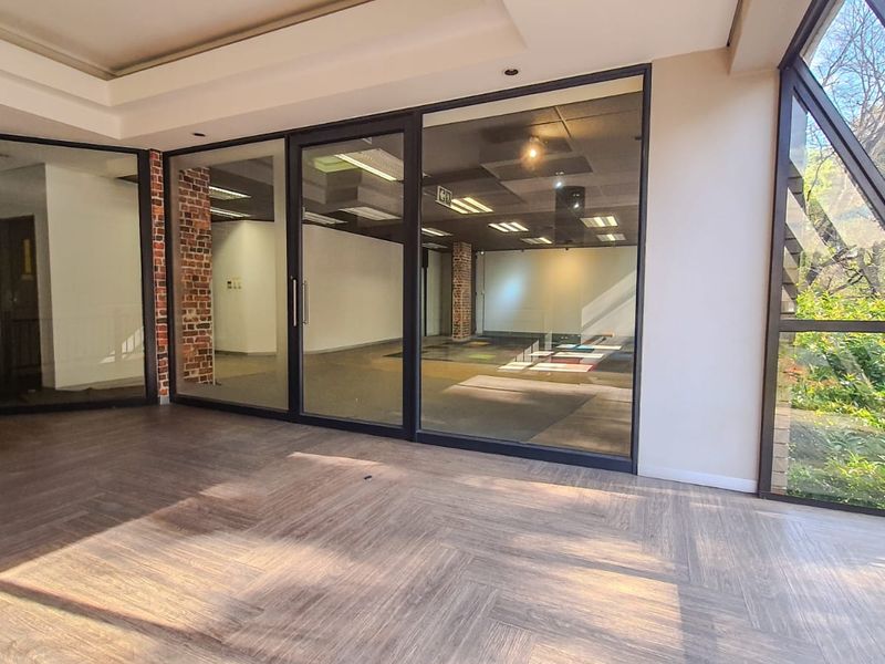 Modern, vacant commercial office space featuring herringbone flooring, exposed brick accents, and large glass partitions providing excellent natural light and an open, professional atmosphere.