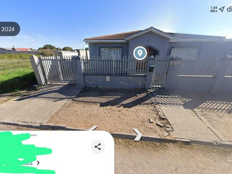 Front exterior view of a house featuring a perimeter wall, metal gate, and paved driveway area showing signs of wear.
