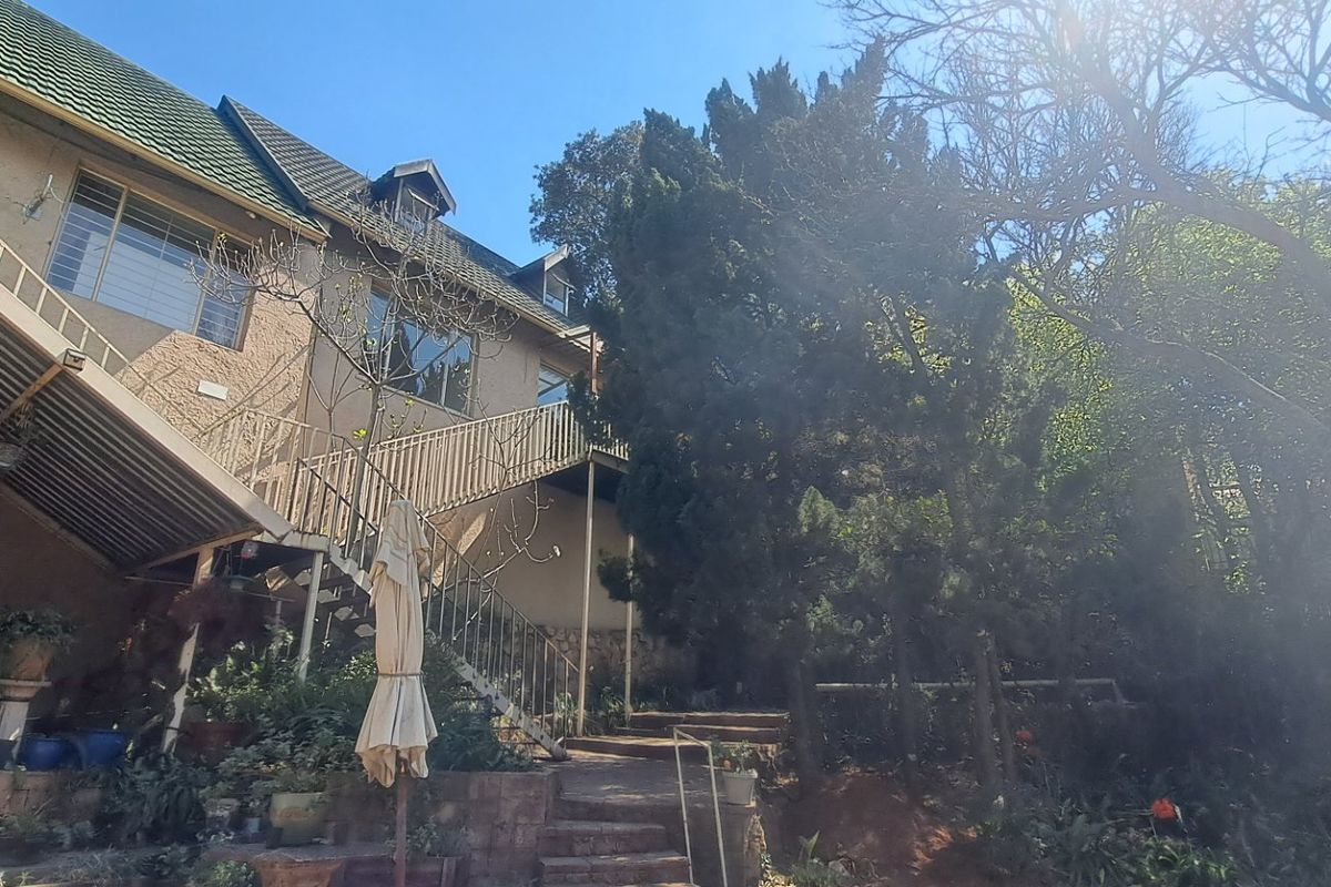 Rear view of the property featuring a multi-level exterior staircase, balcony, and landscaped garden area with mature trees.