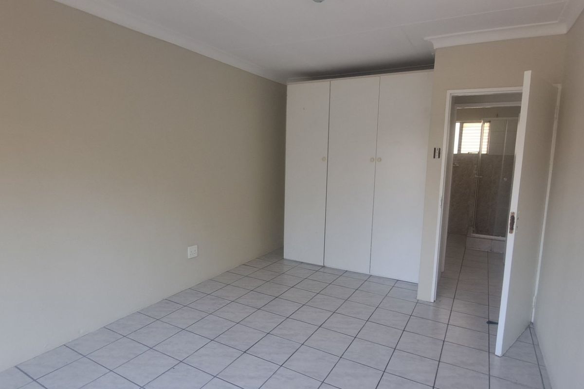 A clean, empty bedroom featuring neutral tiled flooring, built-in cupboards, and direct access to an en-suite bathroom.