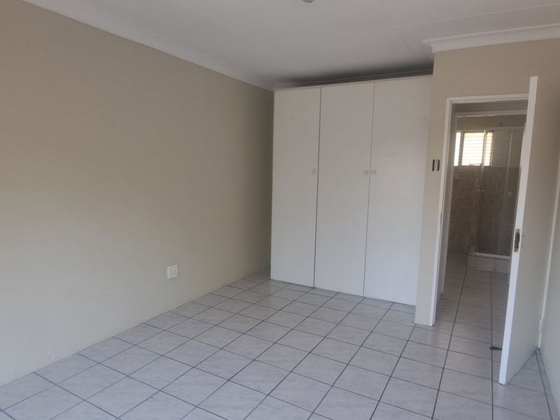A clean, empty bedroom featuring neutral tiled flooring, built-in cupboards, and direct access to an en-suite bathroom.