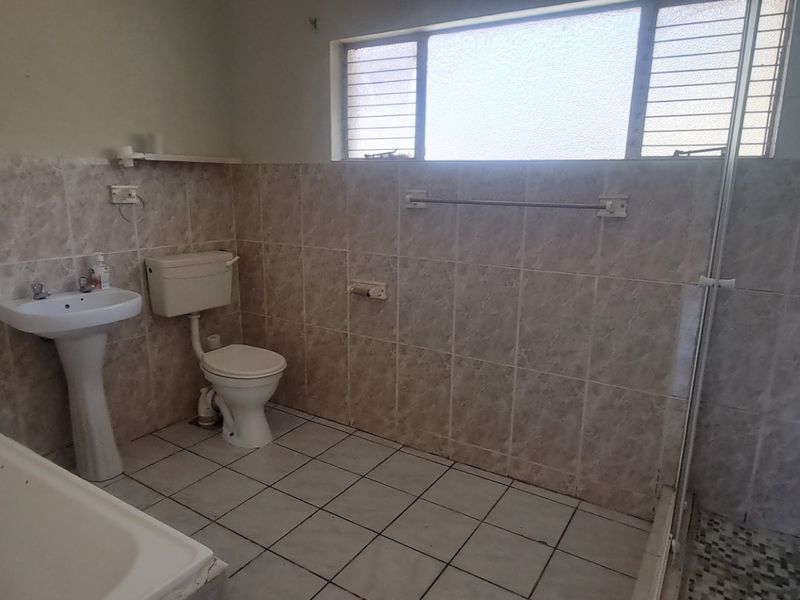 A functional bathroom featuring a bathtub, separate shower enclosure, pedestal basin, and toilet with neutral wall and floor tiling.