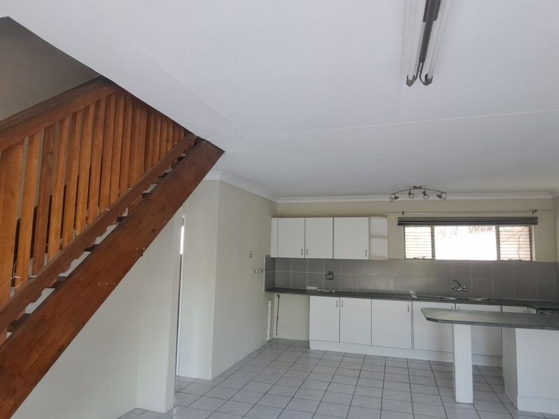 Open plan kitchen area featuring tiled flooring, built-in cabinetry, a breakfast bar, and an adjacent wooden staircase.