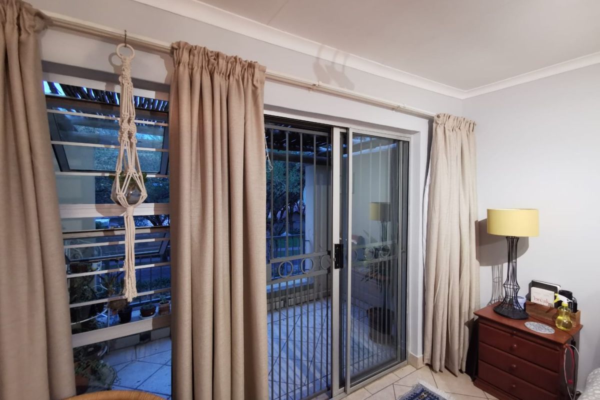 Living area featuring tiled flooring, louver windows, and a sliding glass door with a security gate providing access to the patio.