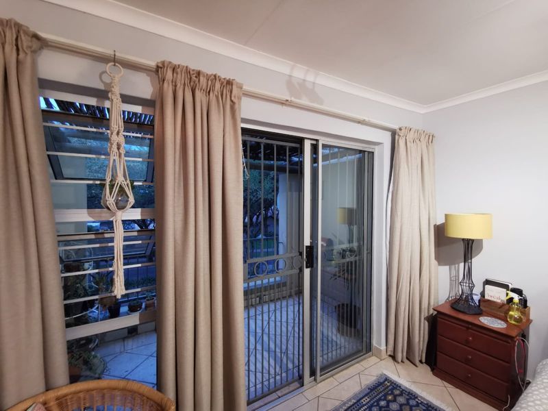 Living area featuring tiled flooring, louver windows, and a sliding glass door with a security gate providing access to the patio.