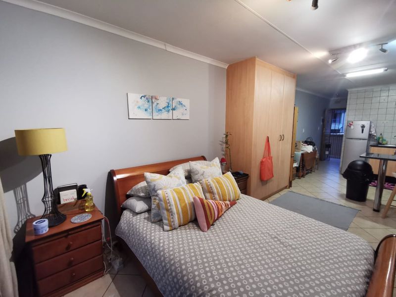 Open-plan bedroom area featuring tiled flooring, built-in wardrobe, and track lighting, seamlessly flowing into the adjacent kitchen space.