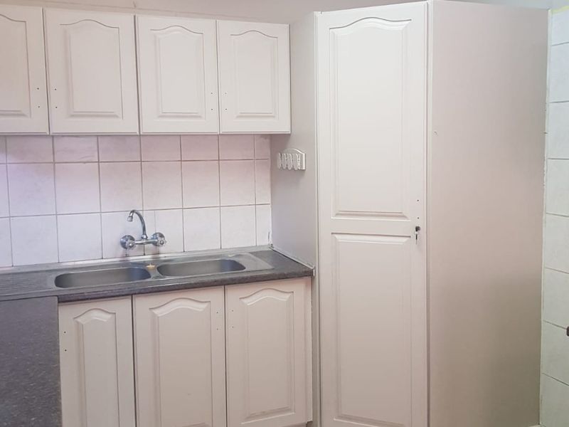 A functional kitchen area featuring built-in cabinetry, a double bowl sink, tiled backsplash, and tiled flooring, offering potential for modern updates.