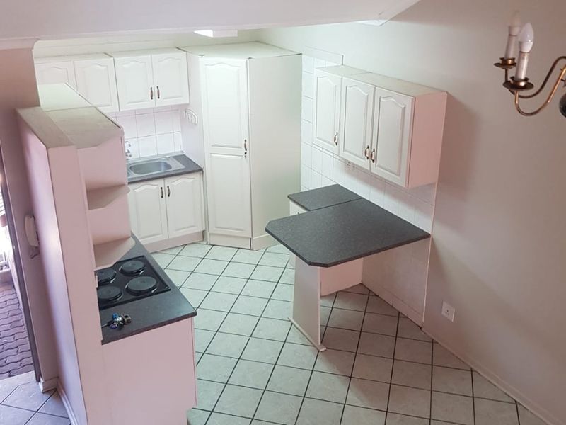 A functional kitchen featuring white cabinetry, dark laminate countertops, an electric hob, and tiled flooring, offering a practical layout with an integrated breakfast nook.