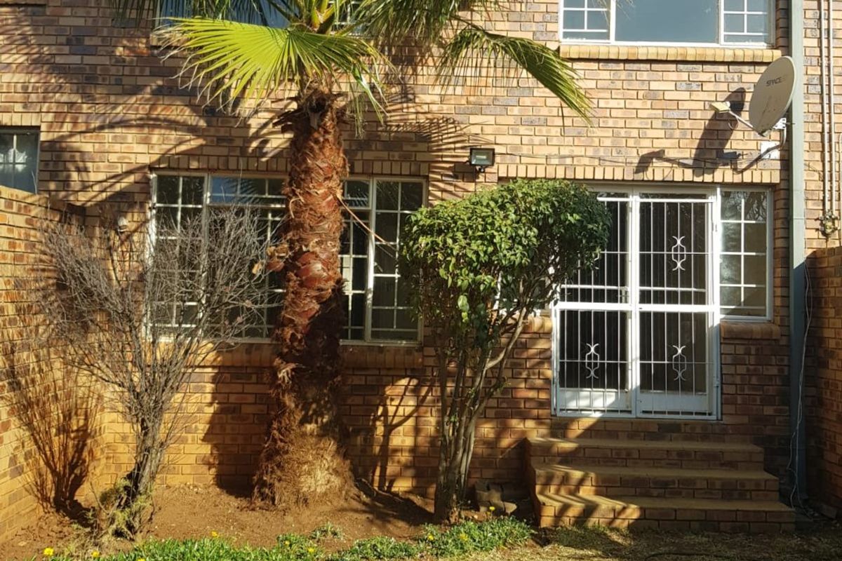 Rear view of a face brick townhouse featuring a small garden, security gate access, and established palm tree.