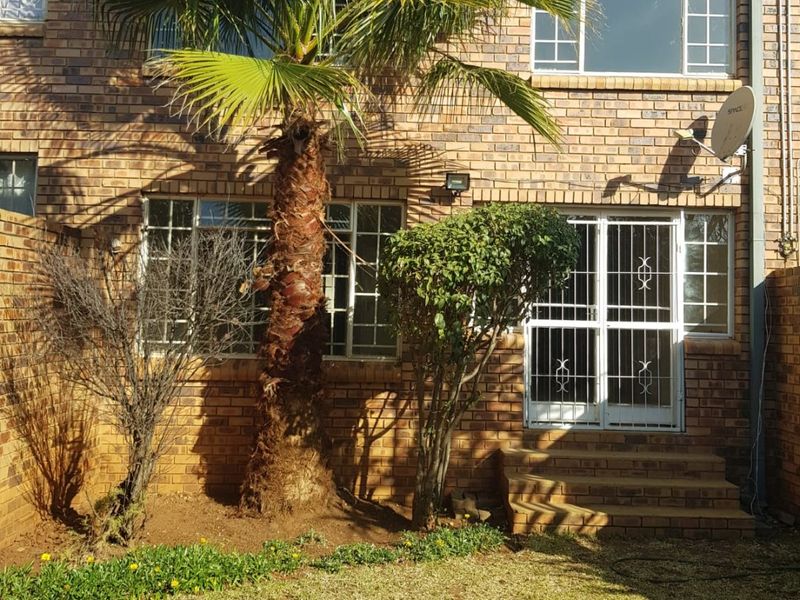 Rear view of a face brick townhouse featuring a small garden, security gate access, and established palm tree.