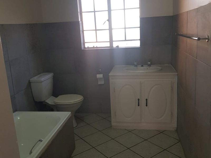 A functional bathroom featuring a built-in vanity, toilet, and bathtub with tiled walls and flooring, offering a clean and neutral space.