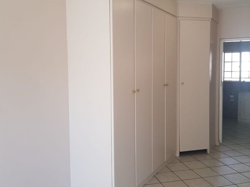 A clean, empty bedroom featuring neutral walls, built-in cupboards for storage, and tiled flooring throughout.