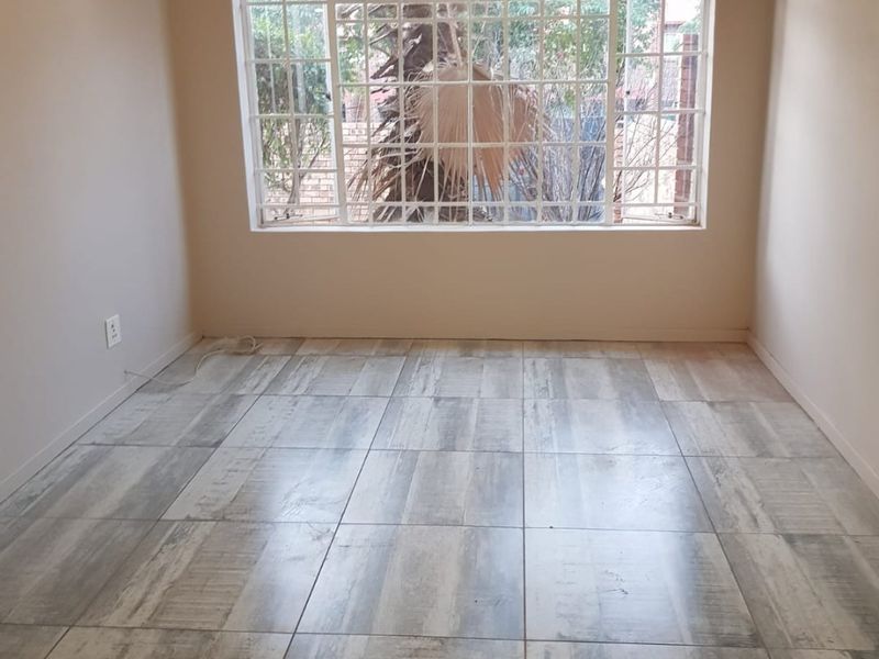 A bright, empty bedroom featuring modern wood-look tiled flooring and a large window fitted with security bars.