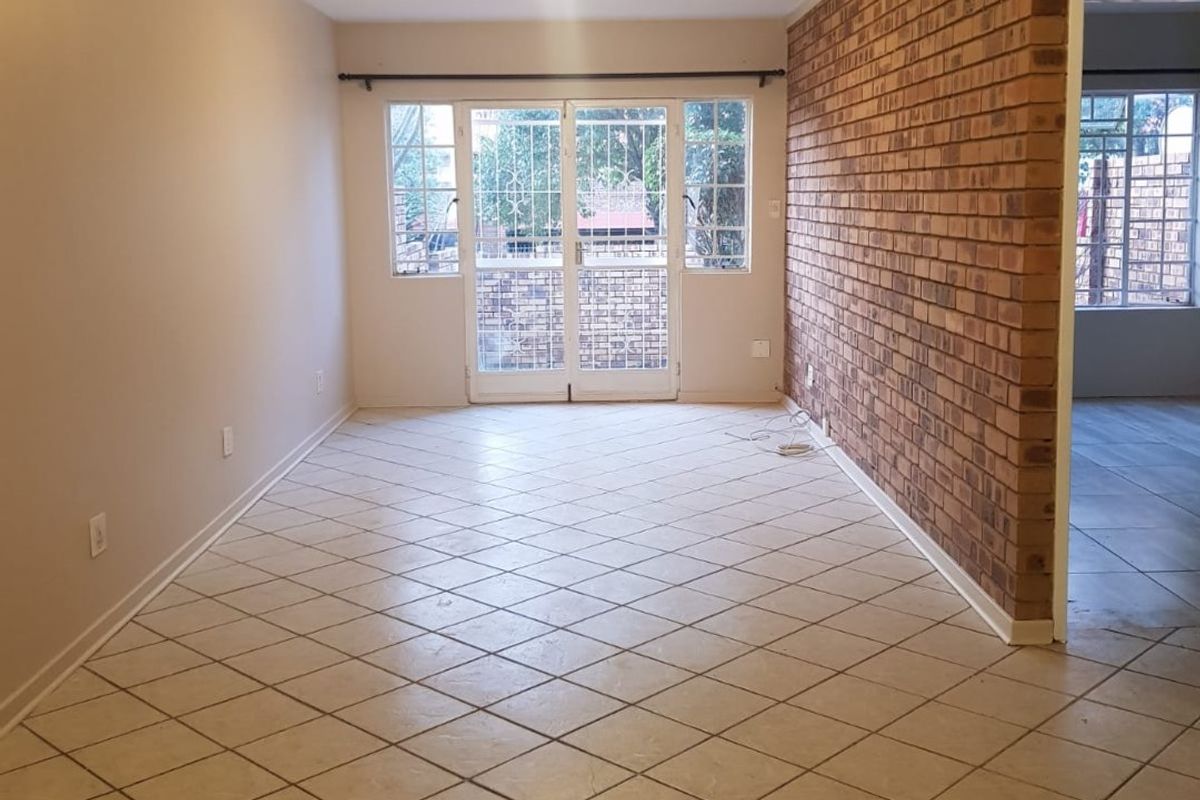 An empty living room featuring an exposed brick feature wall, ceramic tile flooring, and double glass doors leading to the exterior.