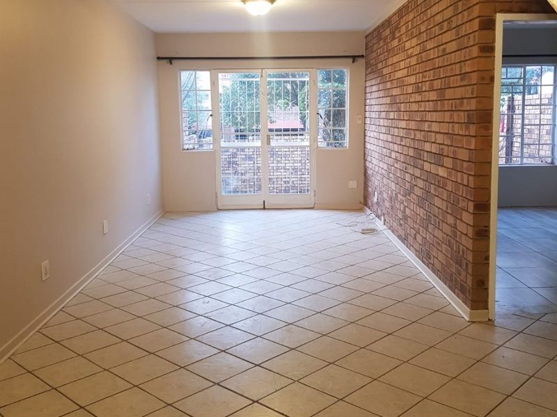 An empty living room featuring an exposed brick feature wall, ceramic tile flooring, and double glass doors leading to the exterior.