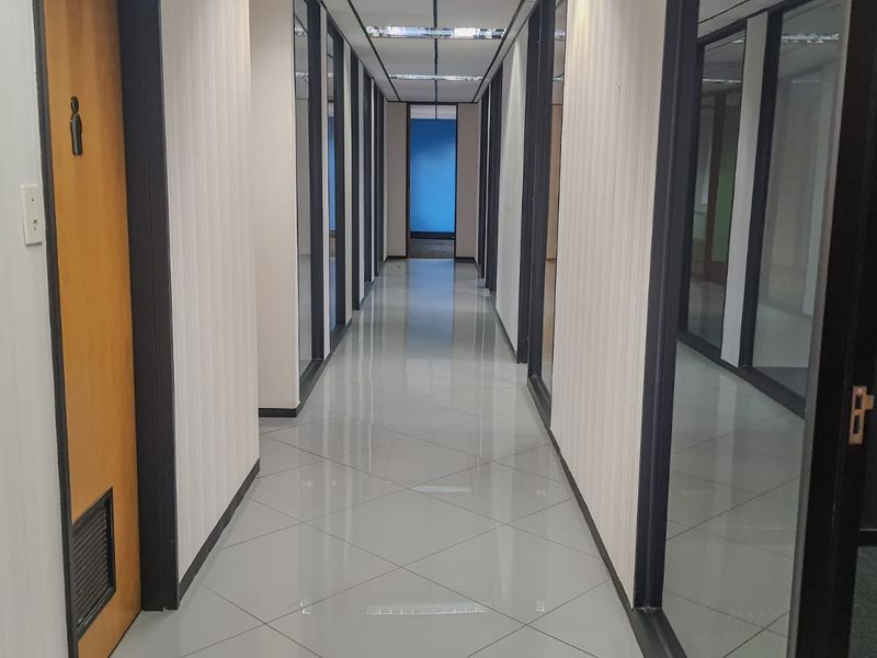 A clean, well-lit commercial office hallway featuring polished tiled flooring, glass-partitioned office entrances, and modern recessed ceiling lighting.