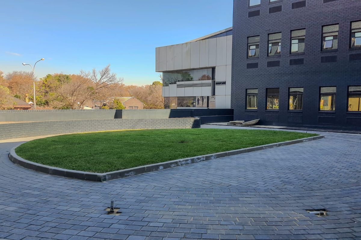 Exterior view of a commercial building featuring a paved driveway, landscaped lawn area, and dark brick facade with modern architectural elements.