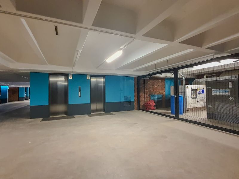 Commercial utility area featuring dual elevators and a secured generator enclosure with concrete flooring and exposed structural ceiling.