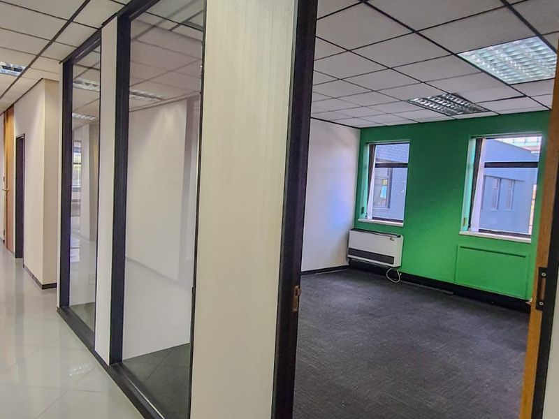 Empty commercial office space featuring glass partitions, suspended ceilings with recessed lighting, carpeted flooring, and a wall-mounted heater.