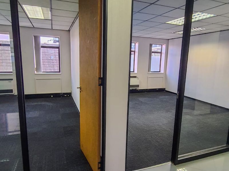 Vacant commercial office space featuring glass partitions, suspended ceilings with integrated lighting, and a combination of carpet and tiled flooring.