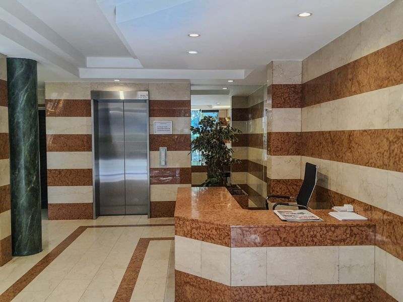 Professional commercial building lobby featuring a built-in marble reception desk, stainless steel elevator access, and high-quality marble wall and floor finishes.