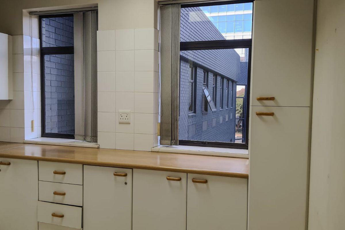 A functional, empty kitchen area featuring white built-in cabinetry, laminate countertops, and tiled backsplash with views of the adjacent building.