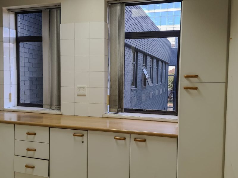 A functional, empty kitchen area featuring white built-in cabinetry, laminate countertops, and tiled backsplash with views of the adjacent building.
