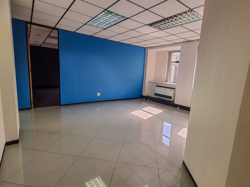 An empty commercial office space featuring polished tile flooring, a suspended ceiling with recessed lighting, and a wall-mounted HVAC unit.