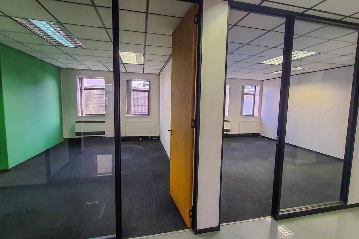 Vacant commercial office space featuring glass partitions, suspended ceilings with recessed lighting, and carpeted flooring, offering a clean and functional layout.