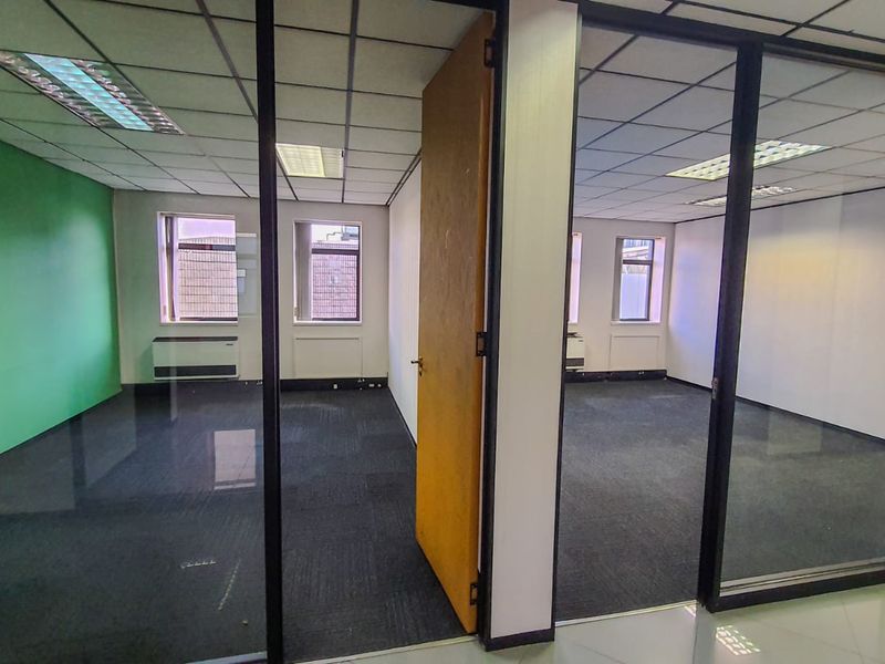 Vacant commercial office space featuring glass partitions, suspended ceilings with recessed lighting, and carpeted flooring, offering a clean and functional layout.