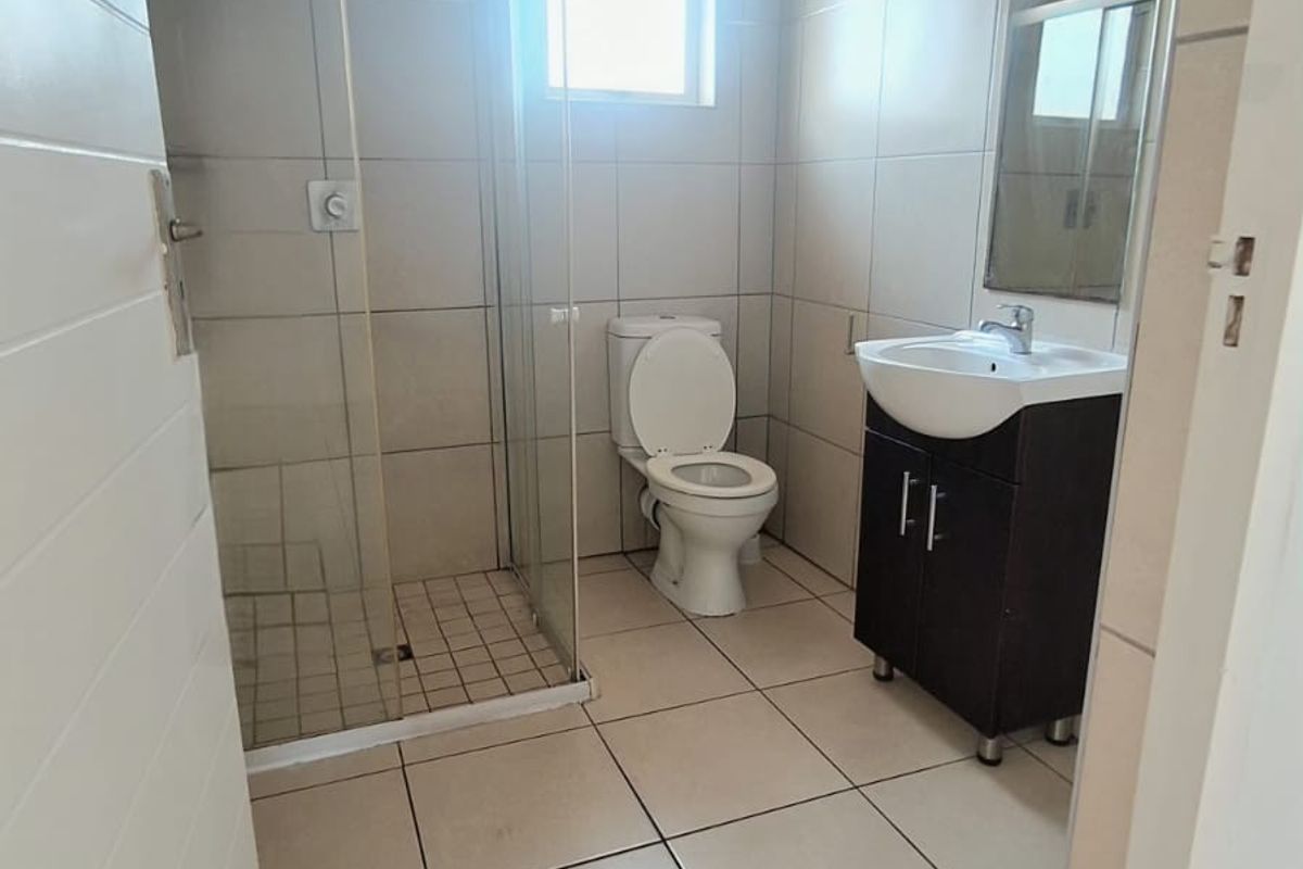 A clean, functional bathroom featuring a glass-enclosed shower, a modern vanity with a washbasin, and neutral floor-to-ceiling tiling.