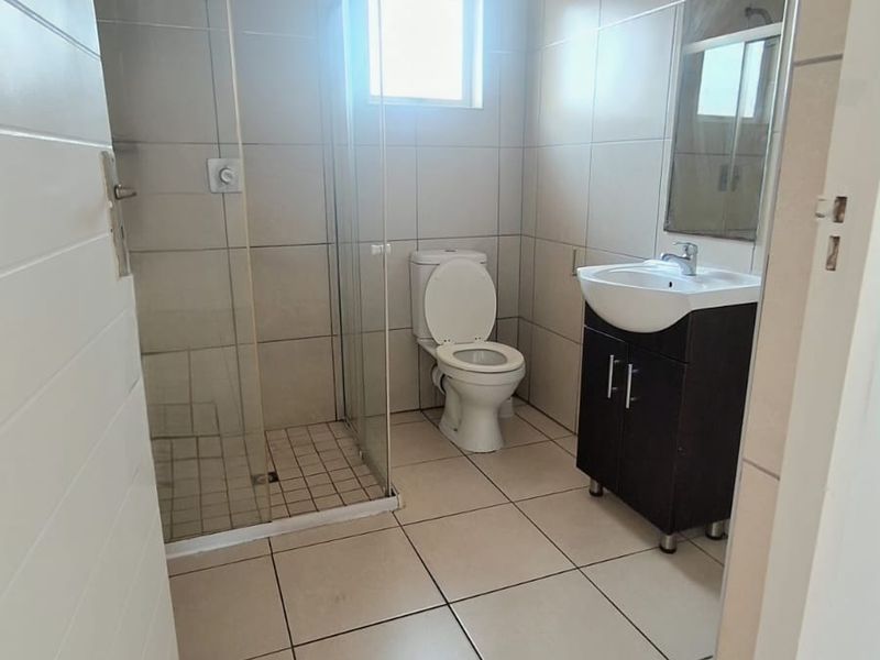 A clean, functional bathroom featuring a glass-enclosed shower, a modern vanity with a washbasin, and neutral floor-to-ceiling tiling.