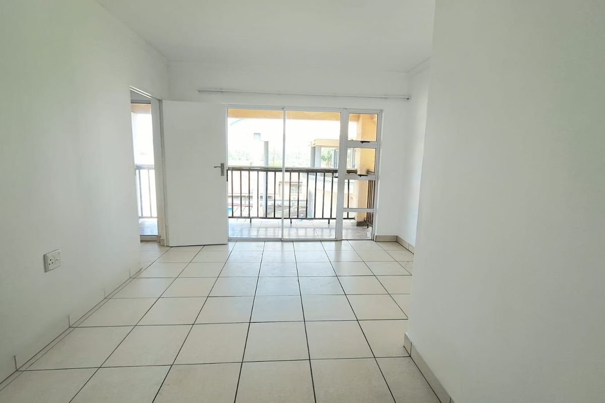 An empty, neutrally painted living area featuring tiled flooring and direct access to a private balcony through a sliding glass door.