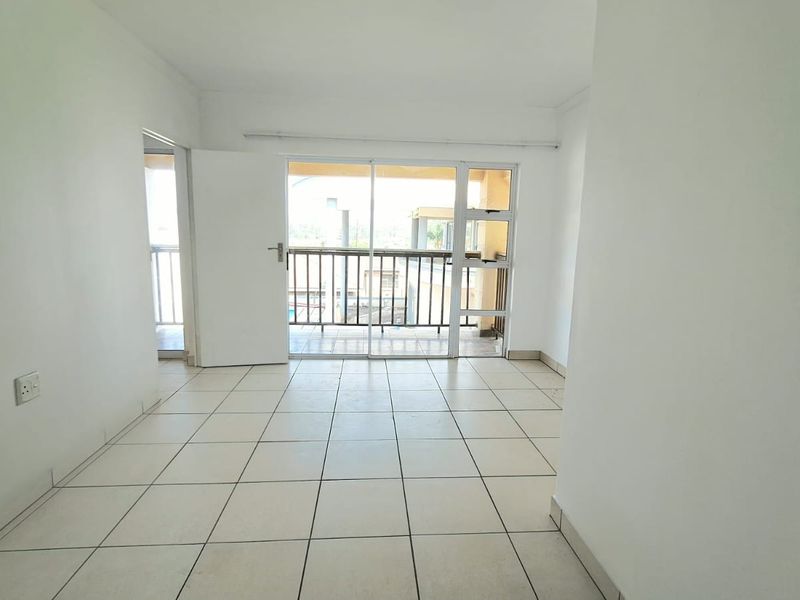 An empty, neutrally painted living area featuring tiled flooring and direct access to a private balcony through a sliding glass door.