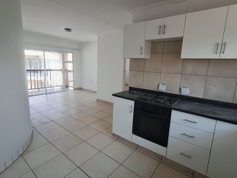 Open-plan kitchen and living area featuring tiled floors, built-in cabinetry, integrated oven and hob, leading to a balcony through sliding glass doors.