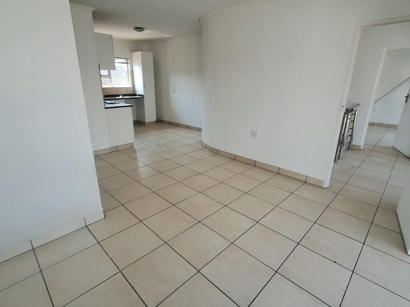 An open-plan living and kitchen area featuring neutral tiled flooring, clean white walls, and a functional kitchen layout with built-in cabinetry.