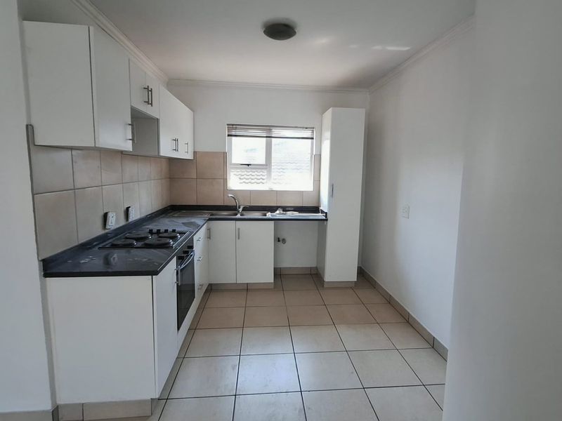 A functional kitchen featuring white cabinetry, dark laminate countertops, a gas hob, built-in oven, and tiled flooring with a neutral splashback.