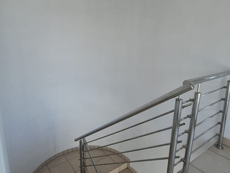 A clean, minimalist staircase area featuring tiled steps and a modern stainless steel balustrade, providing a bright and functional transition space.