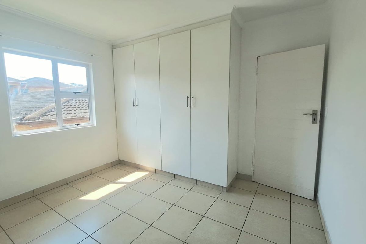 A bright, empty bedroom featuring neutral tiled flooring and ample built-in cupboard storage space.