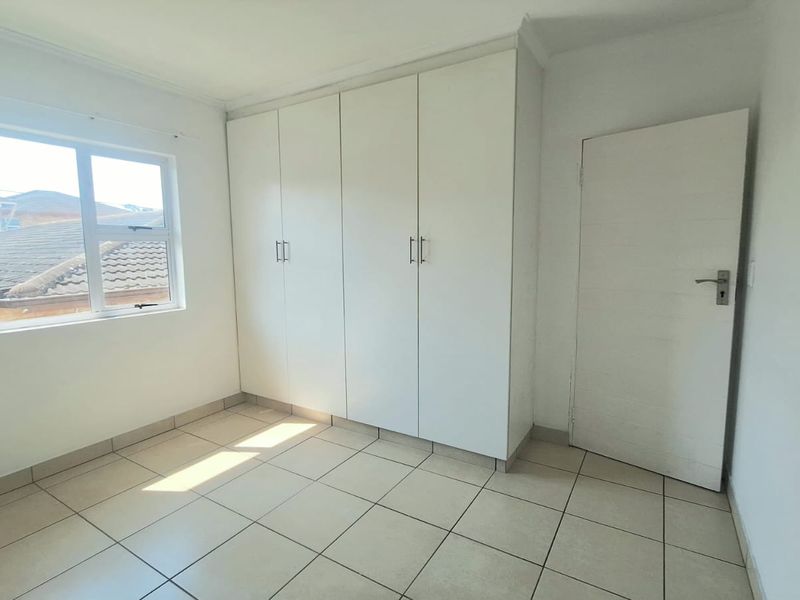 A bright, empty bedroom featuring neutral tiled flooring and ample built-in cupboard storage space.