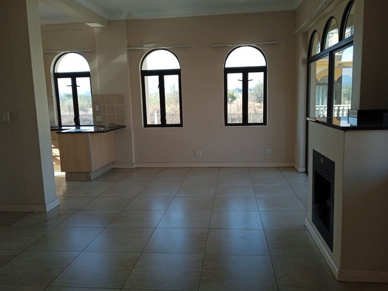 Spacious open-plan living area featuring tiled flooring, arched windows, and a built-in fireplace, seamlessly connected to a functional kitchen space.