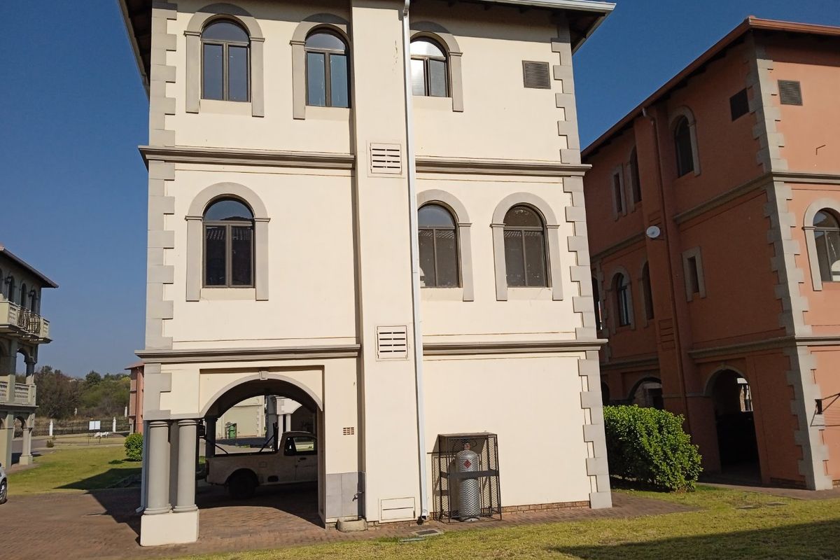A three-story residential building featuring arched windows, a ground-level covered parking area, and a secure external gas cylinder storage cage.
