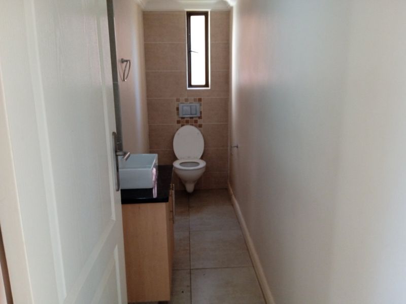 A compact guest bathroom featuring a wall-hung toilet with a concealed cistern, a modern vanity cabinet with a vessel sink, and neutral floor tiling.