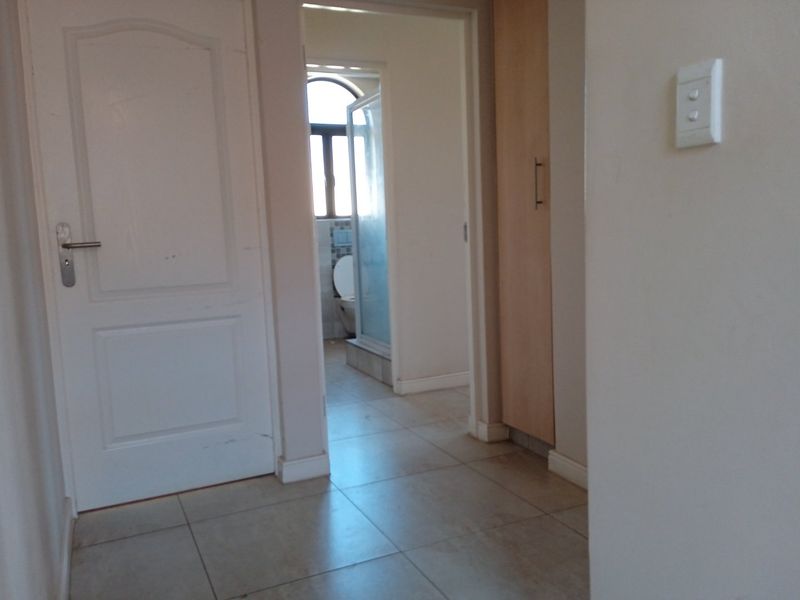 A functional hallway featuring tiled flooring, a built-in cupboard, and access to an adjacent bathroom.