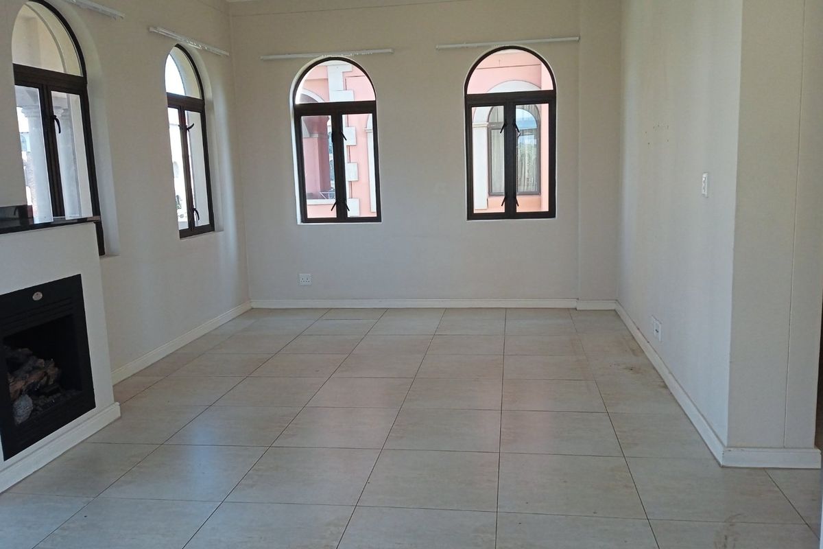 An empty living room featuring arched windows, tiled flooring, and a built-in fireplace, offering a neutral canvas for interior design.