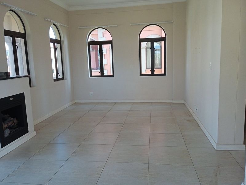 An empty living room featuring arched windows, tiled flooring, and a built-in fireplace, offering a neutral canvas for interior design.
