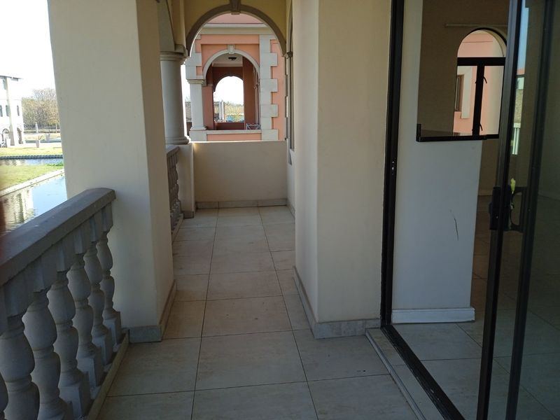 A covered balcony featuring tiled flooring, arched architectural columns, and a balustrade, offering an outdoor space accessible via a sliding glass door.