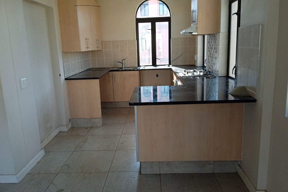 A functional kitchen featuring light wood cabinetry, dark granite countertops, a gas hob, and tiled flooring, offering a clean canvas for updates.